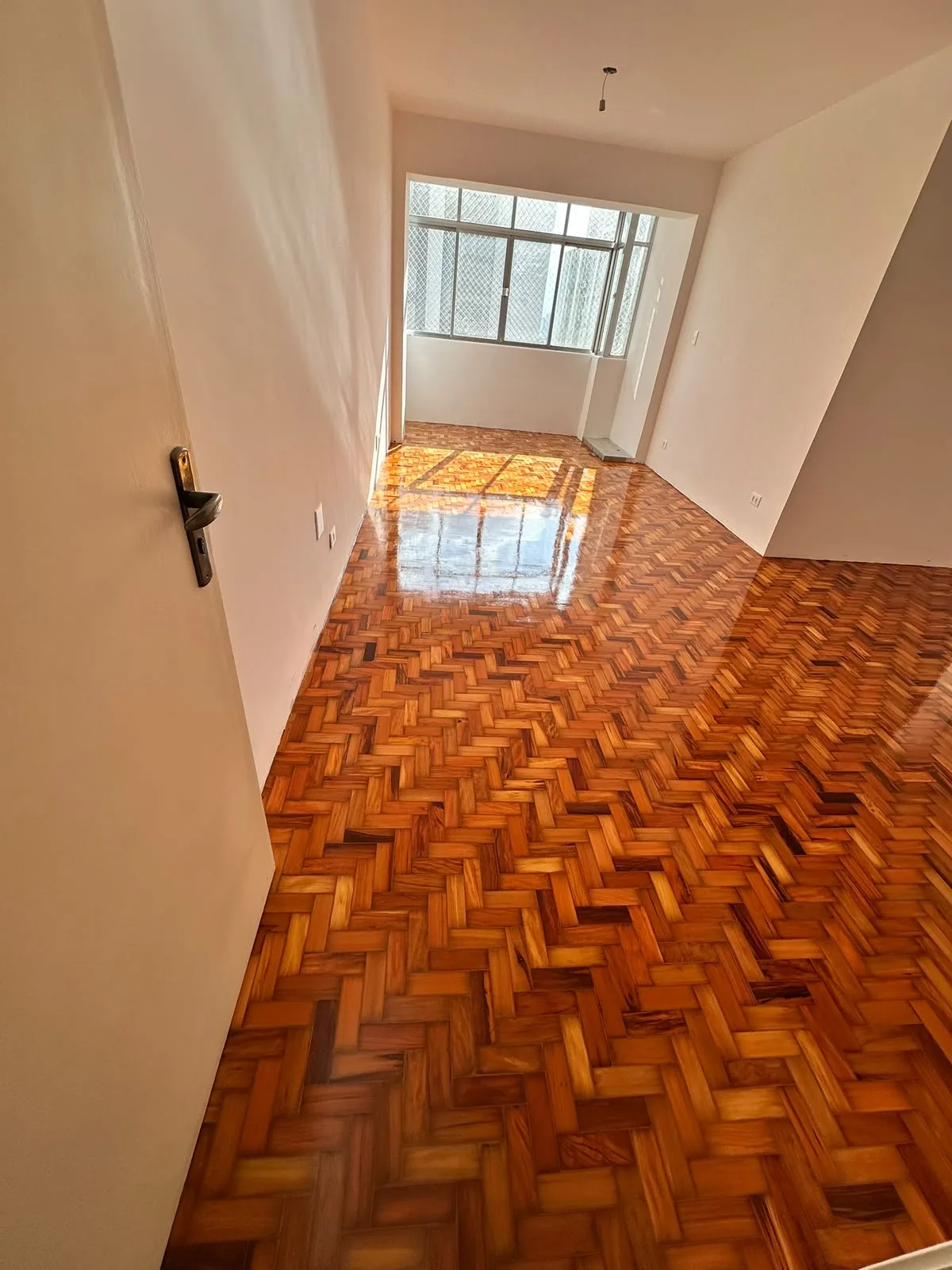 Piso de tacos restaurado em sala comprida, com forte reflexo de luz natural